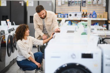 Çift, ihtiyaçları için en iyi seçenekleri seçmeye odaklanarak elektronik mağazasında ev aletlerini inceliyor. Modern alışveriş deneyimi