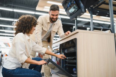 Ev aletleri mağazasında modern fırını seçen mutlu çift mutfak ekipmanları için satın alma kararı alıyor.