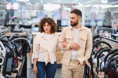 Genç çift ev aletleri mağazasına göz gezdiriyorlar, mükemmel elektrik süpürgesini seçiyorlar ve çeşitli seçenekleri karşılaştırıyorlar.