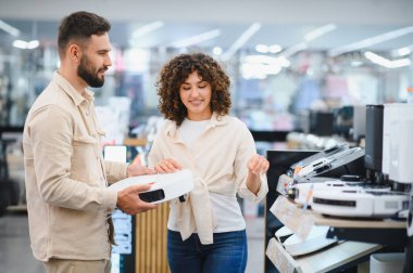 Modern ev aletleri mağazasında birlikte alışveriş yaparken robot elektrik süpürgesini inceleyen mutlu çift.