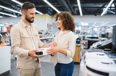 Mutlu çift, elektrikli süpürge tutarken gülümsüyor. Parlak bir ev aletleri mağazasında alışveriş deneyimlerinin tadını çıkarıyorlar.