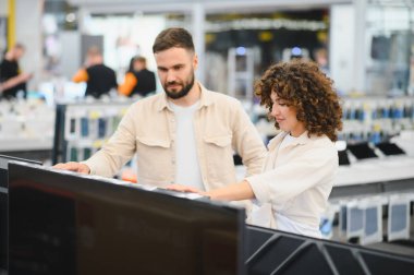 Tüketici elektroniği mağazasında televizyonları karşılaştıran genç bir çift, yeni televizyon alımı hakkında karar veriyorlar.