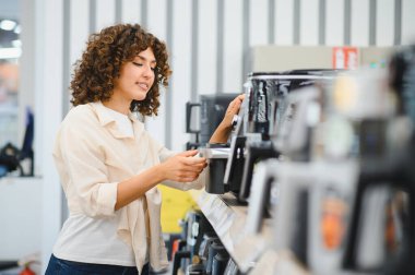 Müşteri, bir ev aletleri mağazasında en iyi seçeneği ararken çeşitli kahve makinelerini karşılaştırıyor ve alışveriş deneyiminin tadını çıkarıyor.