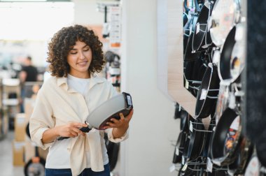Bir ev aletleri mağazasında kızartma tavası seçen genç bir kadın, satın almadan önce kalite ve özellikleri inceliyor