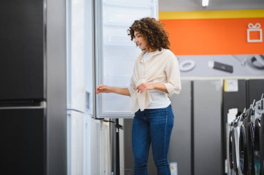 Müşteri buzdolabı kapısı açıyor, ev aletleri mağazasında özellikleri inceliyor, mutfak için satın alma kararı veriyor.