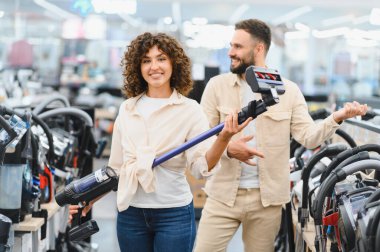 Mutlu çift yeni kablosuz elektrik süpürgesi seçiyor, elektronik mağazasından ev aletleri alıyor.