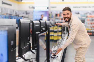 Yeni televizyon setini inceleyen, tüketici elektroniği mağazasında satın alma kararı veren mutlu müşteri