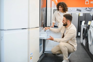 Yeni mutfak güncelleme sürecinin tadını çıkarırken, bir mağazada alışveriş yaparken buzdolabı çekmecesini inceleyen mutlu çift.