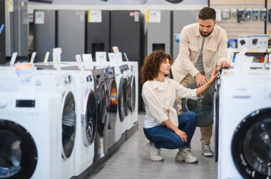 Çift aktif olarak elektronik mağazasında ev aletlerini seçiyor, seçenekleri değerlendiriyor ve satın alma özelliklerini tartışıyor