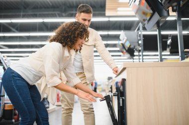 Ev aletleri mağazasında modern fırını inceleyen genç bir çift, mutfakları için satın alma kararı alıyorlar.