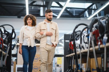 Genç çift bir ev aletleri dükkanına göz atıyorlar, birlikte alışveriş yaparken mükemmel bir elektrikli süpürge seçiyorlar.
