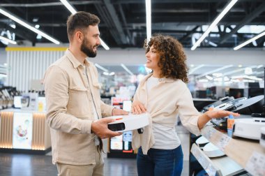 Genç çift yeni bir robot elektrik süpürgesi seçiyor. Elektronik mağazasında farklı modelleri karşılaştırıyorlar.