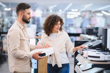 Robot elektrik süpürgesini karşılaştıran, elektronik mağazasından ev aletleri alan genç bir çift.