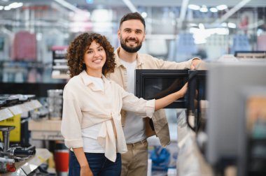 Çeşitli mikrodalga fırınlarda gezinen mutlu çift, bir elektronik mağazasında yeni ev aletleri seçmenin tadını çıkarıyor.