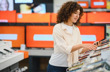 Tüketici elektronik mağazasında akıllı telefonu seçen genç kadın, satın almadan önce özelliklerini ve özelliklerini kontrol ediyor