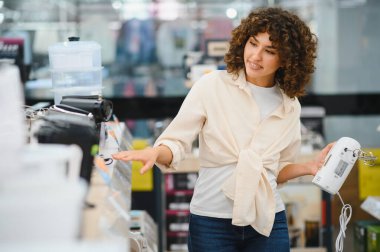 Elektronik mağazasında alışveriş yaparken çeşitli mutfak aletlerini karşılaştıran genç bir kadın, bilgilendirilmiş seçimler yapma sürecinin tadını çıkarıyor.