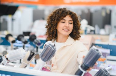 Müşteri bir elektronik mağazasında saç kurutma makinelerini karşılaştırıyor, mükemmel bir saç bakım aleti arıyor.