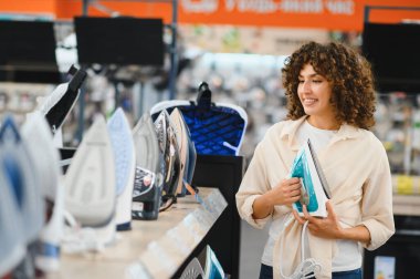 Müşteri ev aletleri mağazasında çeşitli buhar ütülerini karşılaştırıyor, ev ihtiyaçları için satın alma kararları alıyor