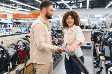 Mutlu çift elektronik mağazasında birlikte alışveriş yapıyor, yeni bir elektrikli süpürge seçiyor, gülümsüyor ve bu deneyimin tadını çıkarıyor.