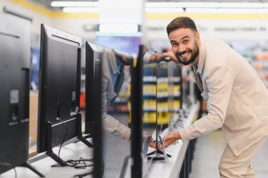 Bir tüketici elektronik mağazasında yeni televizyon setlerini inceleyen gülümseyen bir müşteri satın alma kararı veriyor.