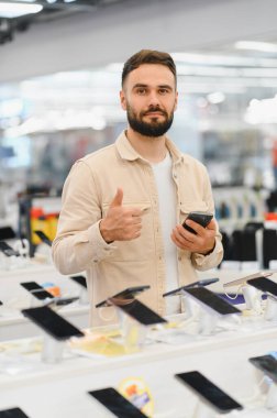 Elektronik mağazasında yeni bir cep telefonu seçerken, alışveriş deneyiminin tadını çıkaran mutlu müşteri başparmağını kaldırıyor.