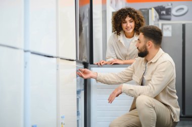 Çift elektronik mağazasından yeni buzdolabı seçiyor ev aletlerini inceliyor, mutfak aletleri için alışveriş yapıyor.