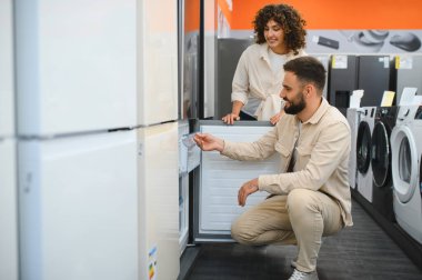 Mutlu çift alışveriş yapmadan önce yeni buzdolabı seçiyor, kompartımanları ve özelliklerini kontrol ediyor