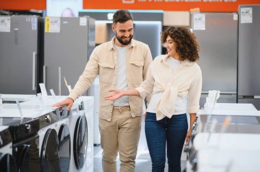 Erkek ve kadın bir elektronik mağazasını keşfederken, ev aletleri konusunda karar verirken seçenekleri tartışıyorlar. Meşgul görünüyorlar ve seçimleriyle ilgileniyorlar.