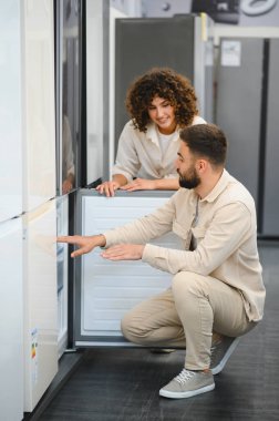 Mutlu çift elektronik mağazasından yeni buzdolabı seçiyor, ev aletlerini inceliyor, mutfak aletleri için alışveriş yapıyor.