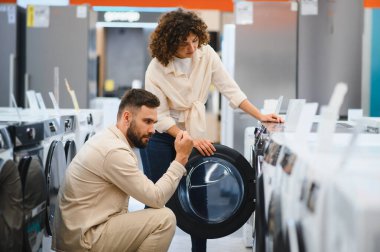 Çift bir elektronik mağazasında çamaşır makinelerini inceliyor, yeni ev aletleri satın alma seçeneklerini inceliyor.