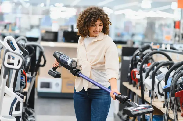 Müşteri, ev aletleri mağazasında çeşitli kablosuz elektrik süpürgelerini karıştırıyor. İhtiyaçları için mükemmel modeli dikkatlice seçiyor.