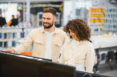 Mutlu çift, tüketici elektroniği mağazasında ev aletleri almak için yeni bir televizyon seçiyor.