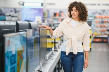 Müşteri, canlı bir perakende mağazasında ev aletleri alırken çeşitli televizyonları karşılaştırıyor ve ev eğlencesi seçeneklerini araştırıyor.