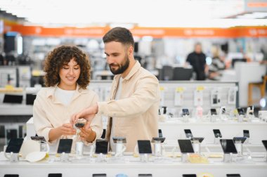 Akıllı telefonları karşılaştıran genç bir çift, tüketici elektroniği mağazasındaki en iyi cep telefonu anlaşmasını arıyorlar.