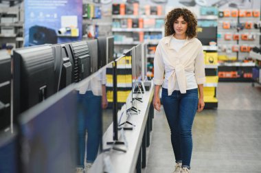 Elektronik mağazası koridorunda yürüyen müşteri, çok çeşitli modern ekran seçeneklerinden dikkatle yeni bir televizyon seçiyor.