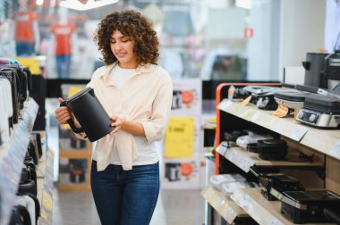 Elektronik mağazasının elektrikli su ısıtıcısını seçen genç kadın, satın almadan önce ürünü inceliyor.