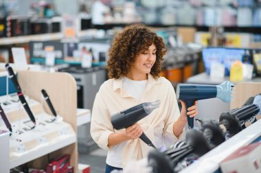 Müşteri iki saç kurutma makinesini karşılaştırıyor, en iyi ürünü ev aletleri mağazasında seçiyor, modern alışveriş yapıyor.