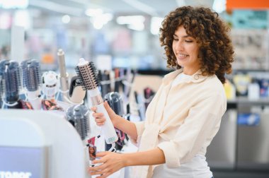 Gülümseyen kadın, canlı ev aletleri mağazasında dönen saç kurutma fırçalarını karıştırıyor.