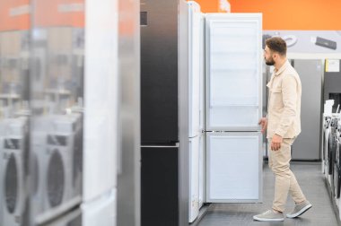 Bir ev aletleri mağazasında buzdolabı seçen bir adam özelliklerini inceleyip satın alma kararı alıyor.