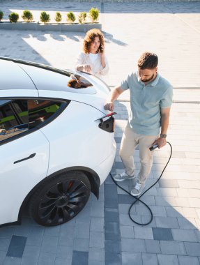 Genç çift, yeşil enerjili sürdürülebilir yaşam tarzının tadını çıkararak elektrikli araçlarını şarj ediyor.