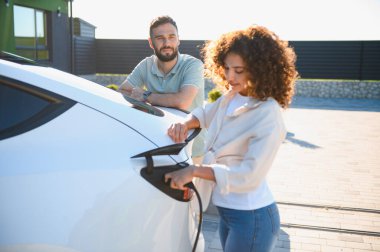 Genç çift elektrikli araçlarını evlerinde şarj ediyor. Çevre dostu ulaşıma ve sürdürülebilir yaşam tarzına bağlılıklarını gösteriyorlar.