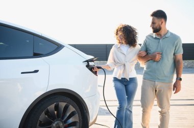 Mutlu çift elektrikli araçlarını evde şarj ediyor, temiz enerji ve ekolojik bilinçli yaşama bağlılıklarını gösteriyor.