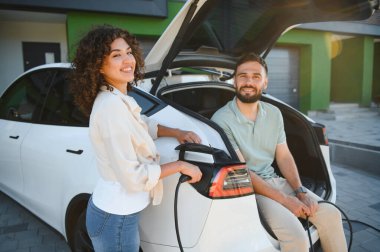 Mutlu çift elektrikli araçlarını evde şarj ediyor, çevre dostu ulaşım ve sürdürülebilir yaşam tarzlarına bağlılıklarını sergiliyorlar.