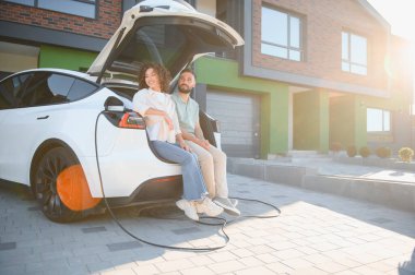 Çift, elektrikli araçları modern evlerinde şarj olurken, rahat ve çevreci bir yaşam tarzı sergiliyor.