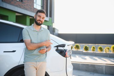 Adam modern binanın dışında şarj olurken elektrikli arabayı gösteriyor.