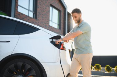 Gülümseyen adam şehir ortamında elektrikli aracı şarj ediyor