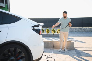Dışarıdaki şarj istasyonuna elektrikli araba bağlayan adam.