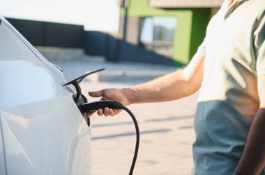 Şarj istasyonunda elektrikli bir aracın fişini takan kişi.