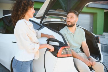 Genç çift elektrikli araçlarını evde şarj ediyor. Çevre dostu ulaşım ve sürdürülebilir yaşam tarzlarına bağlılıklarını gösteriyorlar.