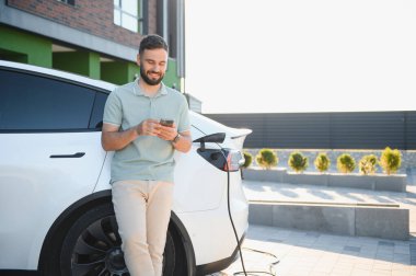 İş adamı evde elektrikli arabayı şarj ederken cep telefonu kullanıyor